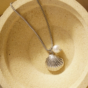 Silver stainless steel shell and pearl pendant necklace on a textured stone display