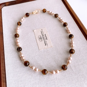 Detail of beaded necklace with pearls, tiger eye stones and gold clasp on linen display