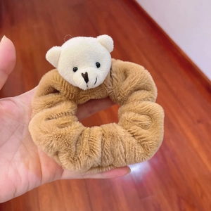 Brown plush hair scrunchie with a cute white teddy bear ornament held over wood background