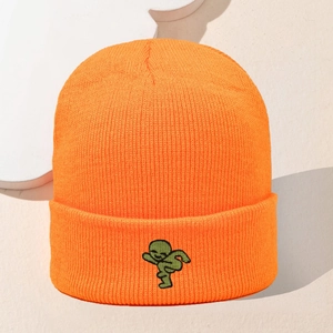 Detail der orangefarbenen Strickmütze mit grüner Alien-Stickerei und dicker Garnstruktur