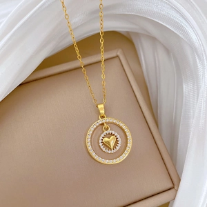 Dettaglio della collana a cuore a doppio strato dorata con pavé di zirconi su portagioie beige