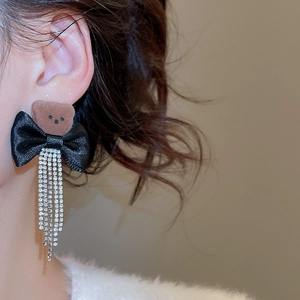 Detail of silver pin earrings with brown flocked bear, black bow and rhinestone tassels
