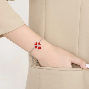 Dettaglio di un bracciale a quadrifoglio rosso su polso di donna in tailleur