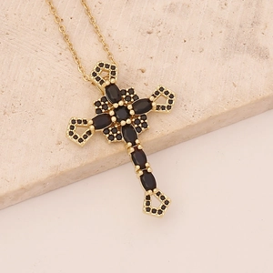 Detailed view of golden cross pendant with black zircon stones on marble background