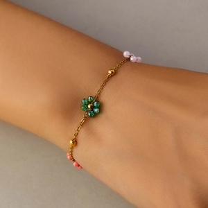 Close-up of beaded flower bracelet with green facets and pink coral beads on wrist