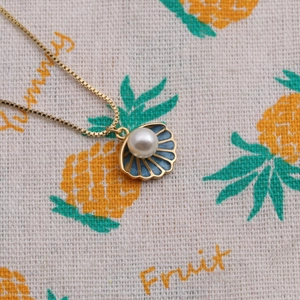 Gold plated necklace with blue enamel shell pendant and pearl on beige fabric