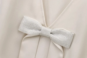 Close-up of V-neck collar detail featuring a sparkling rhinestone bow on cream dress