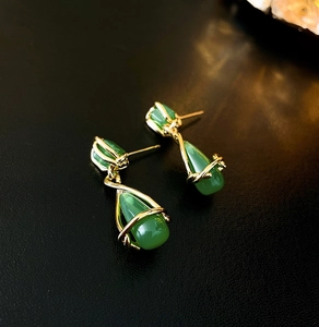 Detailed macro view of gold-plated drop earrings with green gemstones on black background