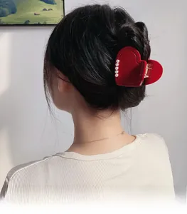 Detail view of a red heart-shaped acetate hair claw clip with pearls on a model back hair