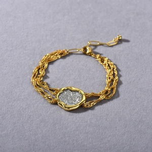 Macro view of woven gold chain bracelet with silver coin pendant and vintage textures