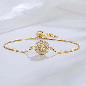 Adjustable gold plated bracelet with a zircon cross pendant on white silk background