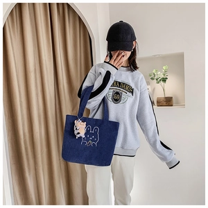 Detail of blue corduroy tote bag with rabbit embroidery and cow plush charm accessory