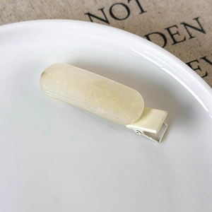 Close-up of a beige jelly duckbill hair clip with gold glitter on a white ceramic tray