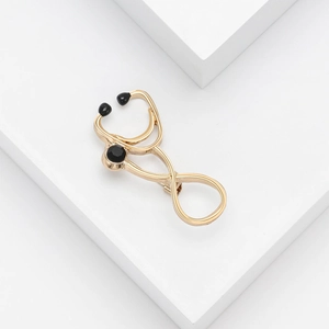 Detailed view of a golden metal stethoscope brooch with black enamel accents on white stand