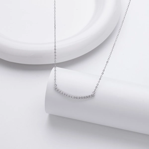 Gros plan d'un collier sourire en argent avec zircons sur un support d'exposition blanc