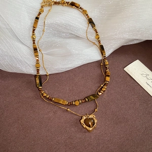 Detail of layered gold necklace with heart tiger eye pendant on a silk fabric background