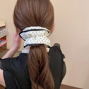 Close-up of a white polka dot scrunchie with black trim on a model's ponytail
