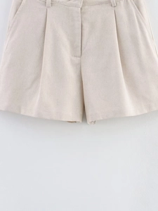 Detail of high-waist beige linen shorts with pleat front design and natural texture