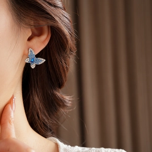 Primer plano detallado de pendientes de mariposa con cristales azules y transparentes