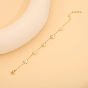 Détail d'un bracelet doré avec des cœurs en nacre blanche sur un fond beige élégant