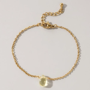 Detail of a thin gold chain bracelet featuring a yellow teardrop gemstone pendant