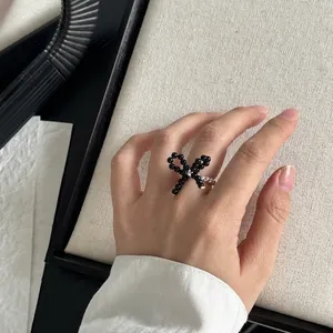 Close-up of a woven black beaded bow ring featuring a pearl and silver bead chain