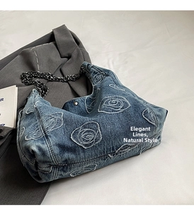 Detailed view of washed blue denim bag with rose embroidery and black metal chain strap