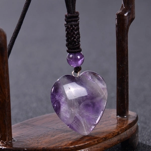 Natural heart-shaped amethyst pendant necklace with brown woven cord on wood display