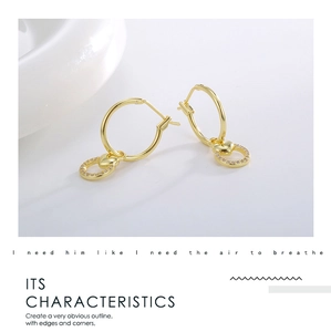 Macro detail of gold-plated hoop earring featuring a hollow heart and zircon micro-pave