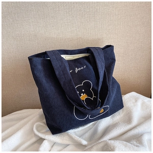 Detail of dark blue corduroy tote bag featuring a cute bear embroidery on fuzzy rug
