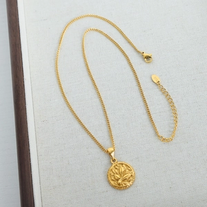 Vintage round floral embossed gold titanium steel pendant necklace on a beige tray