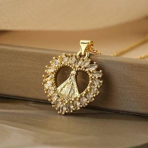 Golden heart pendant necklace with Mary figure and zircon inlay on a textured surface