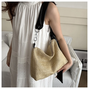 Detail of straw woven shoulder bag featuring a black leather strap and silver chain