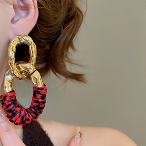 Close-up of geometric gold chain earrings with textured metal and red-black leather details