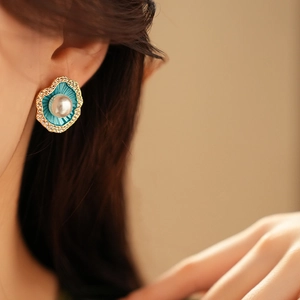 Vue macro de la boucle d'oreille fleur dorée avec émail bleu et perle centrale sur l'oreille