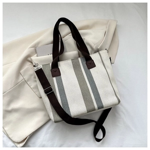 Detail of striped canvas tote with brown handles and adjustable strap on a blazer