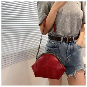 Detail of red vintage shell bag with metal clasp and black chain strap shown on model