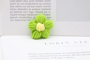 Detail of handcrafted green crochet yarn flower with yellow center on an open book