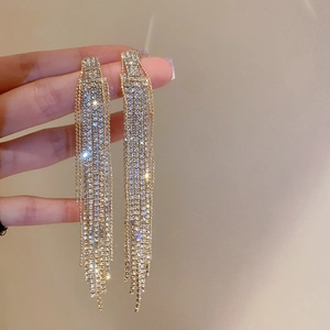 Detailed close-up of sparkling gold tassel earrings with rhinestone studs being held