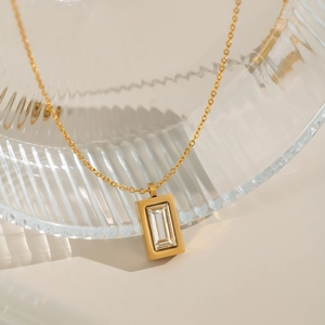 Golden necklace with a rectangular zircon pendant displayed on a clear glass bowl edge