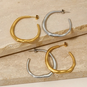 Minimalist large wavy hoop earrings in gold and silver finish on stone background
