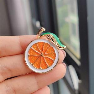 Macro detail of enamel orange slice brooch showing pulp texture and green leaf