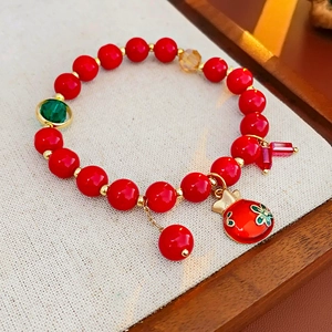 Détail d'un bracelet en perles rouges avec breloque sac de fortune doré et cristaux verts