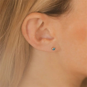 Detail view of a minimalist round blue zircon stud earring on a female ear model
