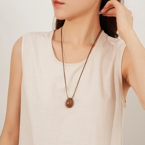 Détail du pendentif ovale marron minimaliste sur un collier en cordon de cire bohème