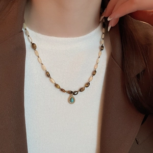 Close-up of beaded necklace with tiger eye stones and turquoise drop pendant on model