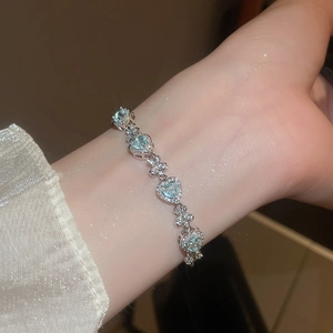 Close-up of light blue heart-shaped gemstone bracelet with floral silver links on wrist