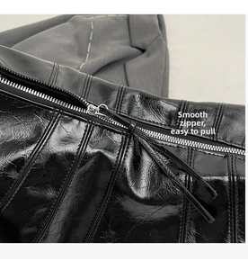 Detail of a smooth silver zipper and glossy black pleated leather texture on a tote bag