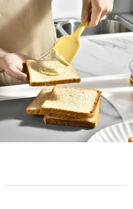 Close-up of a yellow silicone spatula spreading butter on toast in a modern kitchen