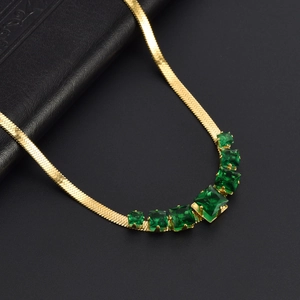 Macro detail of a gold snake chain necklace with five square green gemstones on leather